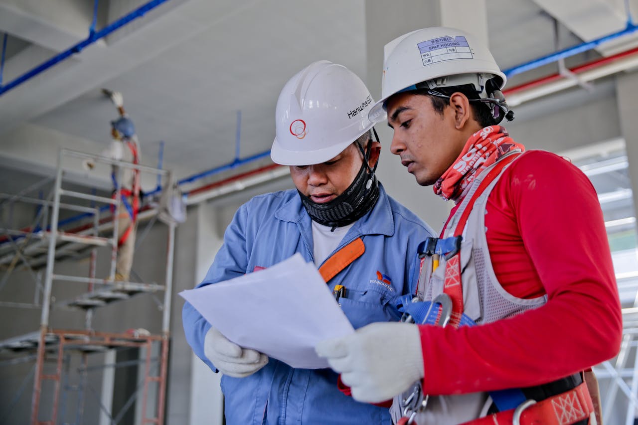 About Two engineers in safety helmets reviewing construction plans at a worksite.